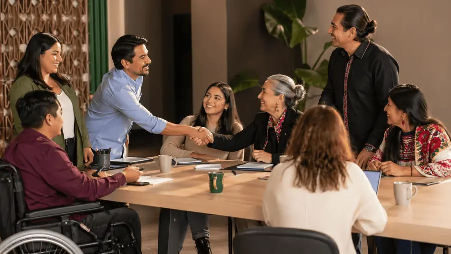 Personas diversas dialogan y se dan la mano en una mesa de trabajo